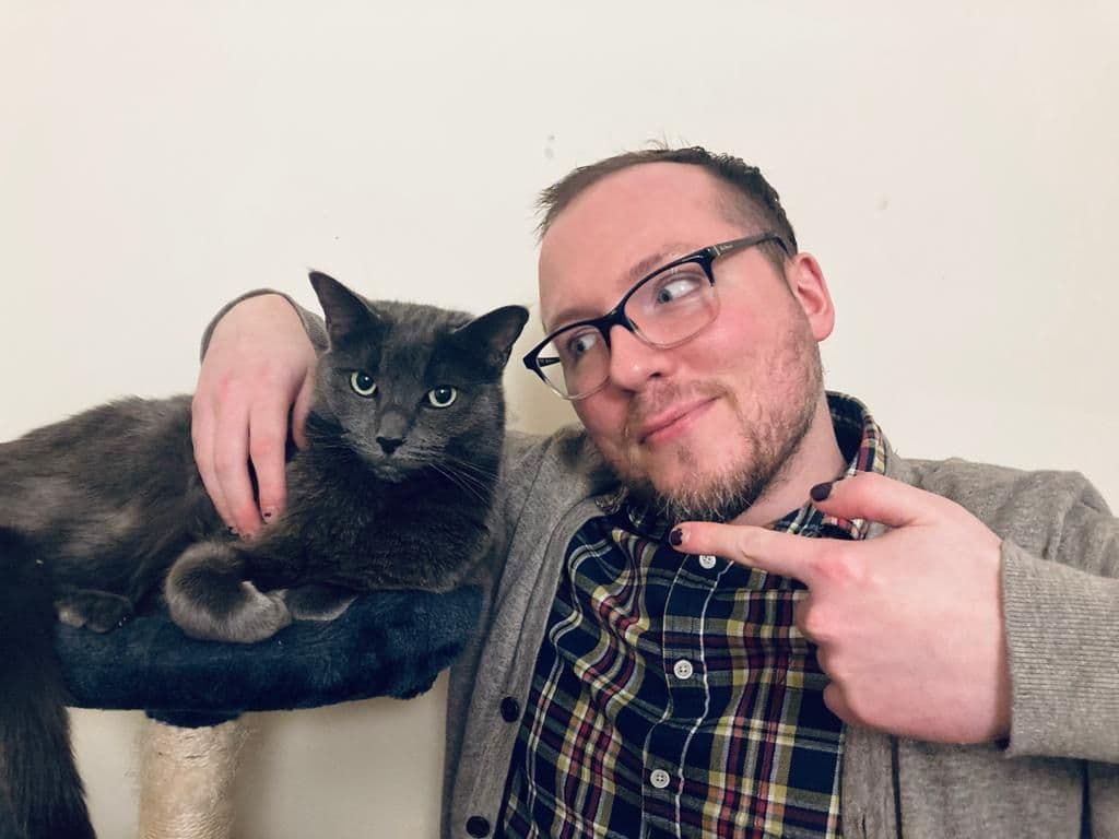 The author with his arm around Borscht, a large Russian Blue Cat, pointing a finger at him as if to say 'this guy right here'.